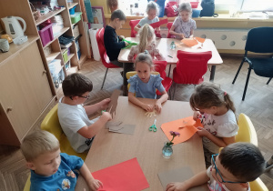 Dzieci przy stolikach odrysowywują i wycinają dłonie
