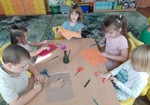 Pięcioro dzieci przystoliku odrysowywują i wycinaja dłonie