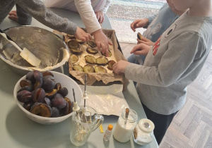 Kilkoro dzieci układa śliwki na cieście