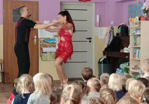 Kilkoro dzieci stoi z instrumentami, a obok stoja tancerze