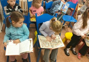 Dzieci siedząc na krzesłach oglądają książki